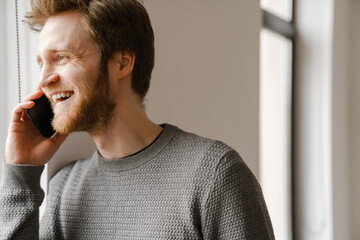 Ginger young man talking on mobile phone while standing indoors