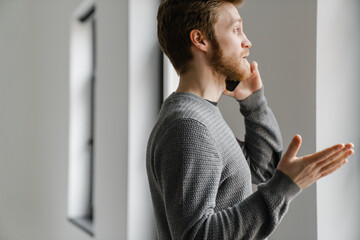 Ginger young man talking on mobile phone while standing indoors