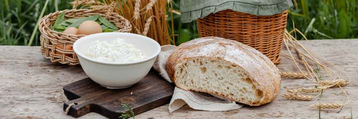 Concept of natural organic products from the local farm. Homemade bread, fresh milk, eggs, cottage cheese. Simple food. Wooden background, outdoors. Close up, copy space. Banner