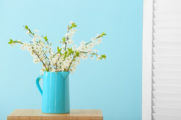 Jug with beautiful blooming branches on color background
