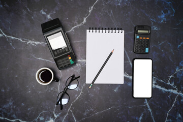 Above view empty notepad, glasses, coffee cup, smart phone and payment terminal on marble background.