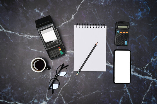 Above view empty notepad, glasses, coffee cup, smart phone and payment terminal on marble background.