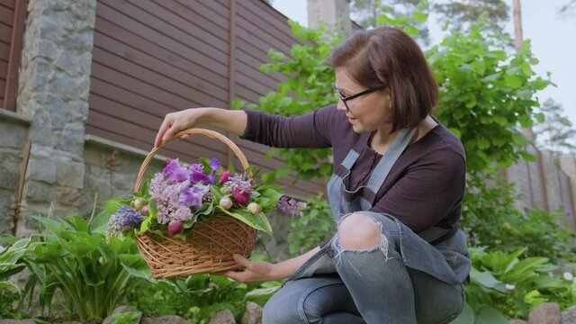 Woman gardener, florist in garden with basket of fresh plucked garden spring flowers