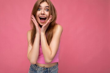 Young delightful attractive dark blonde female person with sincere emotions isolated on background wall with copy space wearing stylish pink top. Positive concept