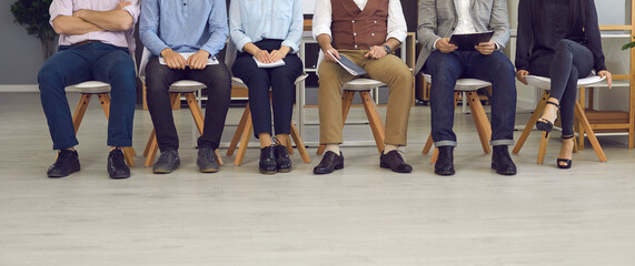 Group of business people sitting on chairs in modern office, legs and feet on floor low section shot. Job seekers in formal clothing line up waiting for interview. Staff members in corporate workshop - Powered by Adobe