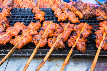 Grilled chicken with wooden stick on charcoal grill at street market in Bangkok, Thailand. Chicken is the main subject