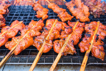 Grilled chicken with wooden stick on charcoal grill at street market in Bangkok, Thailand. Chicken is the main subject