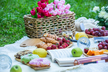 Outdoors picnic in a lush green park with a tasty croissant, fruits, donuts and wine on grass. Summer picnic on the blanket.