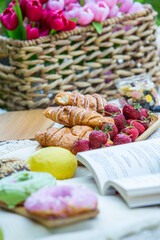 Outdoors picnic in a lush green park with a tasty croissant, fruits, donuts and wine on grass. Summer picnic on the blanket.