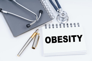 On the table are a stethoscope, a pen and a notebook with the inscription - obesity