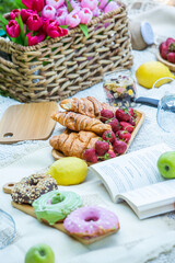 Outdoors picnic in a lush green park with a tasty croissant, fruits, donuts and wine on grass. Summer picnic on the blanket.
