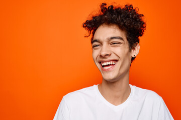 young guy in white t-shirt curly hair smile orange background