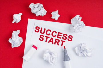On a red background lies crumpled paper, a marker and a sheet of paper with the inscription - SUCCESS START