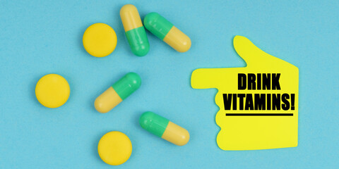 On a blue background, there are pills and a hand-sticker with the inscription - Drink vitamins
