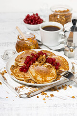 delicious pancakes with berries and honey for breakfast on white table, vertical