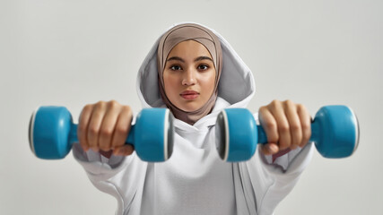 Young arabic woman in hijab holding dumbbells