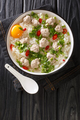 Easy Thai rice soup with meatballs Khao tom moo closeup in the plate on the table. Vertical top view from above