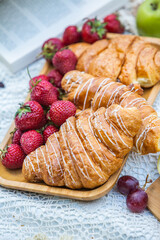 Outdoors picnic in a lush green park with a tasty croissant, fruits, donuts and wine on grass. Summer picnic on the blanket.