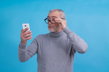 The man has vision problems, squints his eyes while trying to see the mobile phone, takes off his...