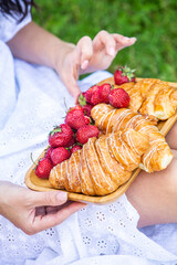 Outdoors picnic in a lush green park with a tasty croissant, fruits, donuts and wine on grass. Summer picnic on the blanket.