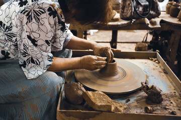 An Asian woman potter shapes a piece of pottery.