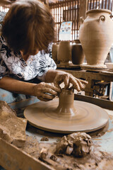 An Asian woman potter shapes a piece of pottery.
