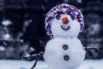 Smiling snowman in hat , dark background, snowfall