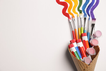 Waffle cone with different paints and brushes on white background, top view. Space for text