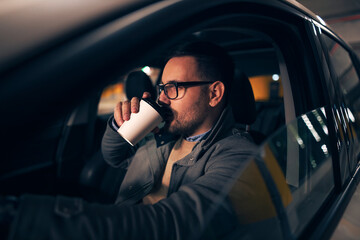 Handsome guy driving at night and drinking coffee