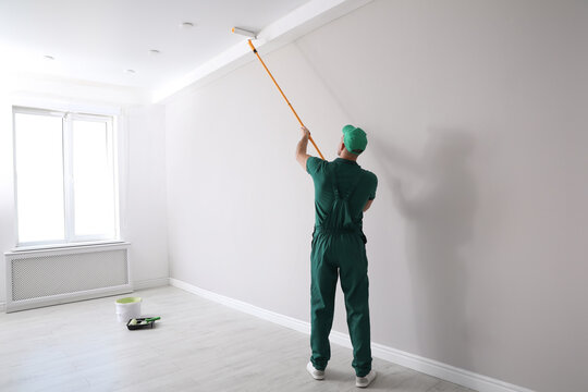 Man painting ceiling with roller in room, back view