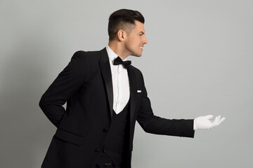 Handsome butler in elegant uniform on grey background