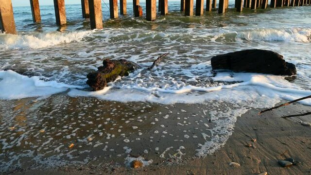 against the background of piles from the pier small sea waves on a pebble beach