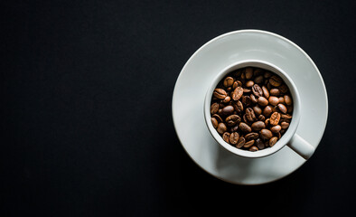 Flat lay of roasted coffee beans in white coffee on black background with copy space 