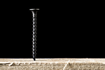 Photo with dark metal screw screwed into wooden board in close-up isolated on black with space for...