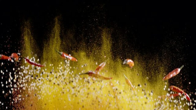 Mixture of ground spices, assorted peppers, salt and small red chili peppers slowly rise and fall against a black background. 300fps