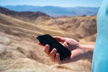 A man holds a smartphone with a blank screen in the desert in Death Valley