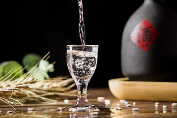 chinese liquor is poured into a glass from a bottle on wood background