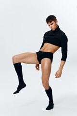 a man athlete in shorts, a sweater and socks raised his leg up on a light background
