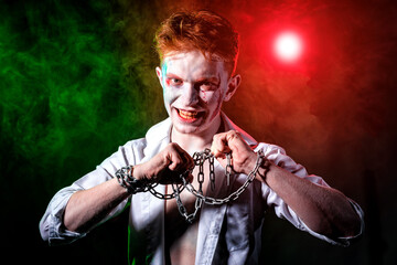Aggressive psycho with blood on his face and chain in his hands against the background of smoke,...