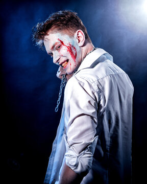 Aggressive maniac with blood on his face looks from behind the shoulder on a dark background