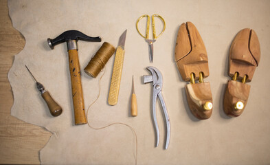 shoe tools, a hammer, wooden blocks, an awl, threads, scissors lie on a piece of leather, indoors....