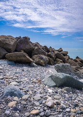 Seaside landscape with pebbles and breakwater stones in the foreground and clear horizon and sky in the background. Summer leisure activity, tourism, travel and vacation.