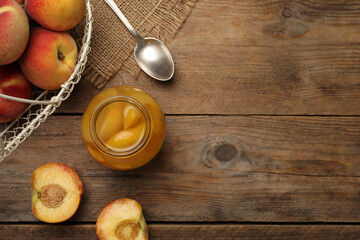 Canned peach halves in glass jar on wooden table, flat lay. Space for text