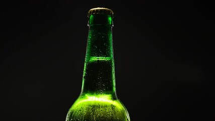 Green beer bottle spins in dark.