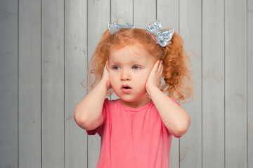 Frustrated and distressed redhead little girl in casual pink t shirt hold hands on head and feeling pain, tired or upset