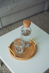 Home interior. A glass bottle with water, a glass, a rattan wicker tray on a coffee table.