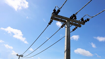 High voltage cables on concrete poles. Transmission line with insulators and support arms on cement pole on white cloudy blue sky background with copy space. Selective focus