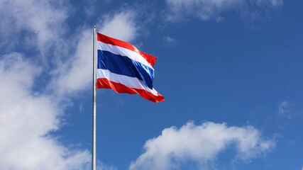 Thailand flag is fluttering in wind. Symbol of Thai nationality waving beautifully against blue sky background with white clouds.