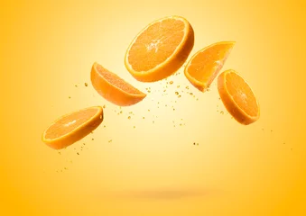 Gordijnen Orange fruit slices flying and dripping on colored background © winston