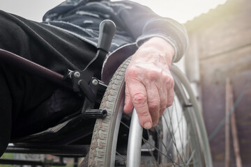 Senior disabled person hand holding pushing wheel close up view, handicapped paralyzed elderly adult grandmother invalid patient moving sitting on wheelchair, disability equipment mobility concept